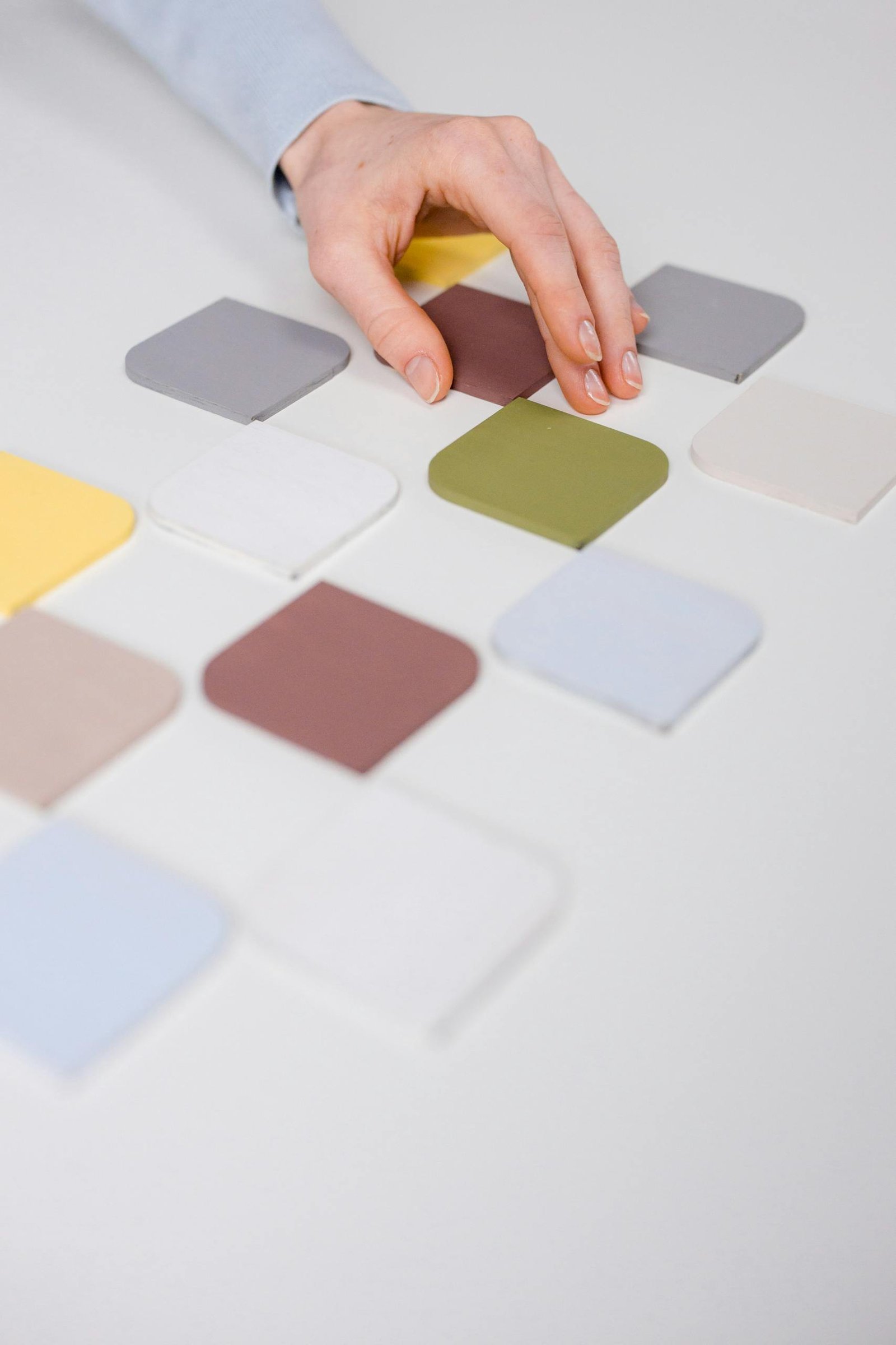 Close-up of a hand arranging diverse color swatches on a white table.