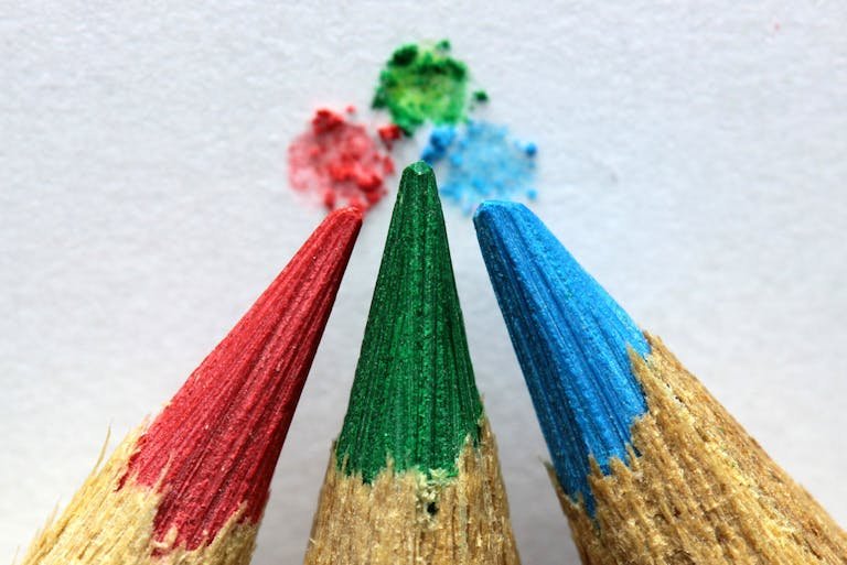 Close-up of red, green, and blue colored pencils with color pigments on paper.