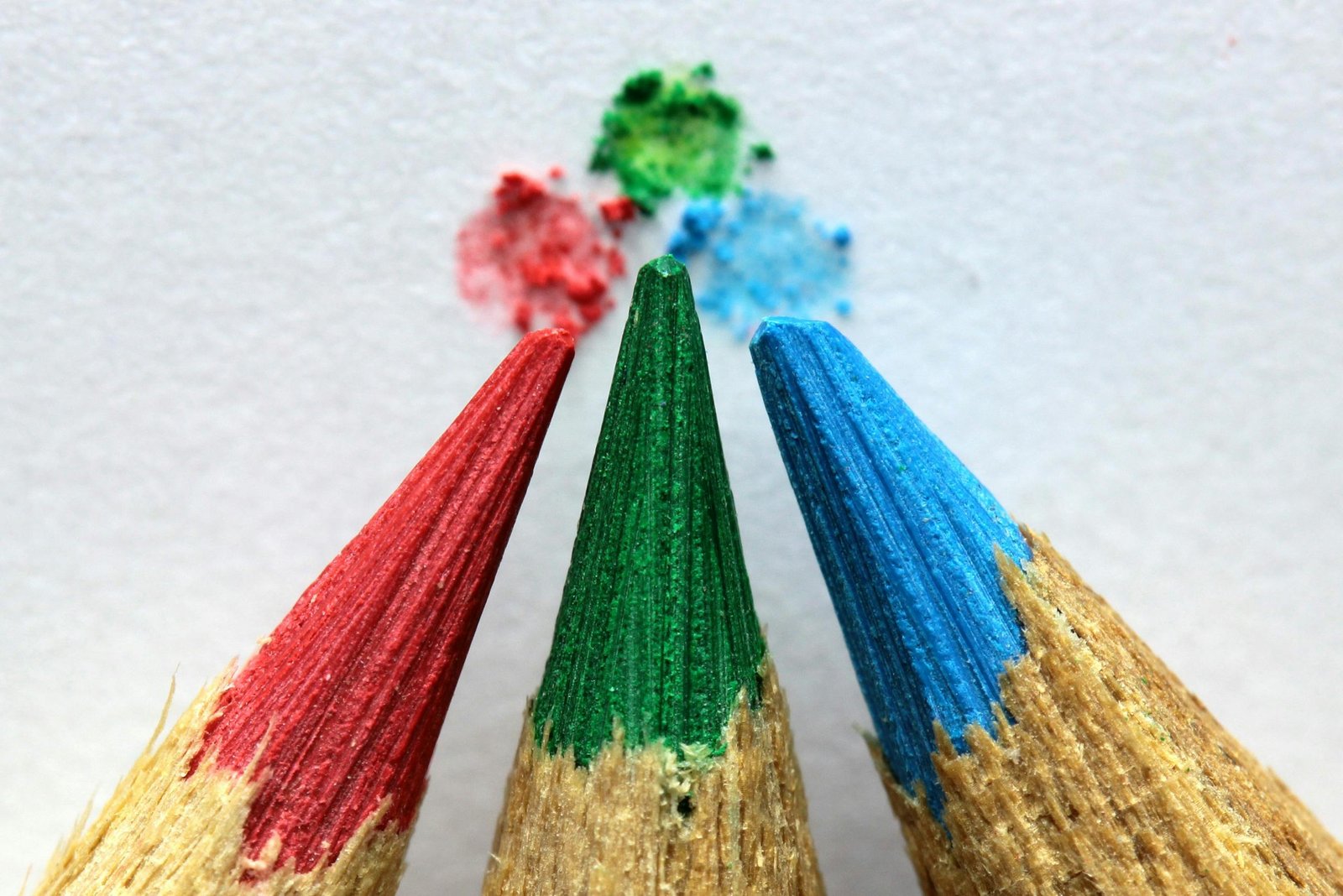 Close-up of red, green, and blue colored pencils with color pigments on paper.